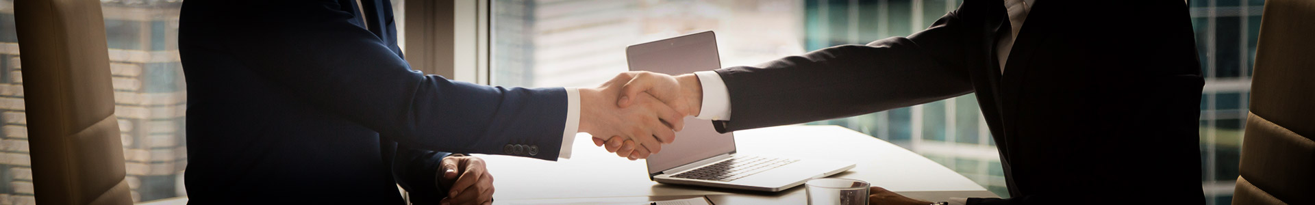 two businessmen shaking hands together at a desk in a office in business skyscraper